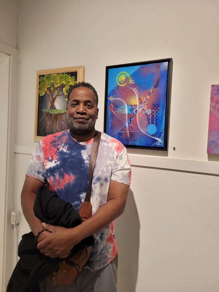 Christopher Van Loan Sr stands in front of his painting hanging in a gallery