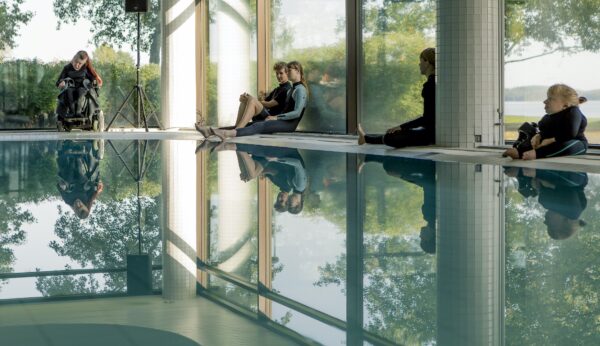 Dancers sit around the edges of an indoor pool