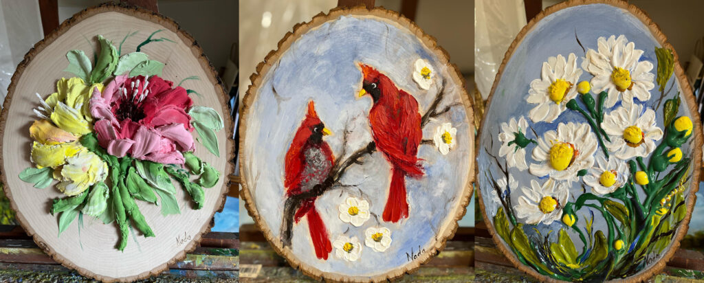 3 wood panels with low relief paints on each of them. On the left, a yellow and red flower stand out from the green foliage that surrounds them. In the center, two red cardinal birds glance at each other as they sit on a tree branch. On the right, White daisies with bright yellow centers reach up to the sky as they grow from the bottom corner.