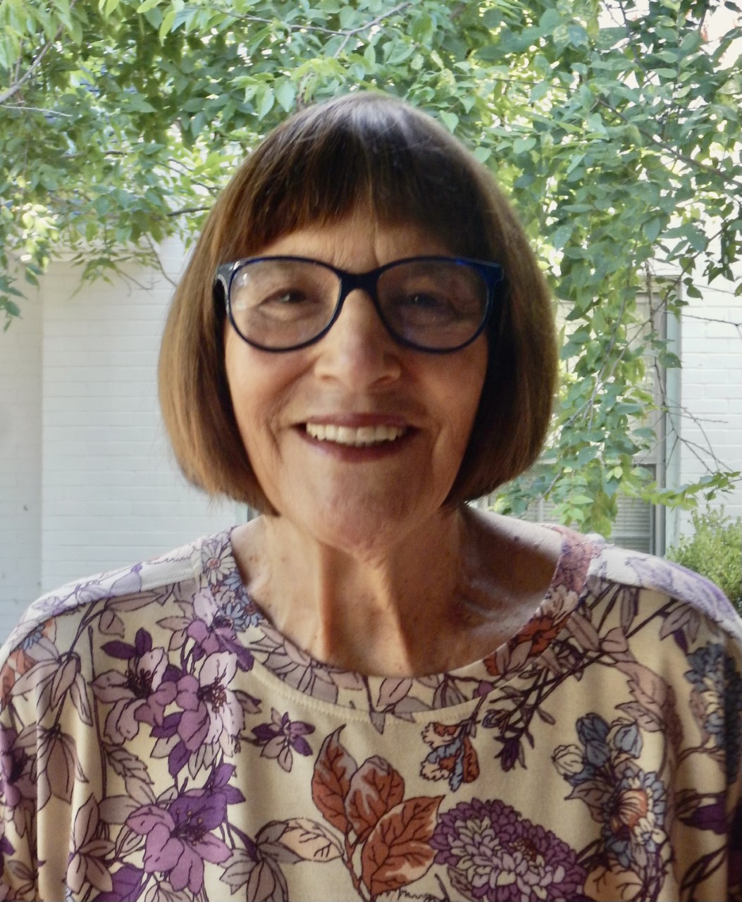 Patti Falconer smiles for the camera while standing under a tree.